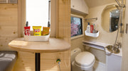 Supplier application illustration of the white storage box beside an RV table and in a bathroom.